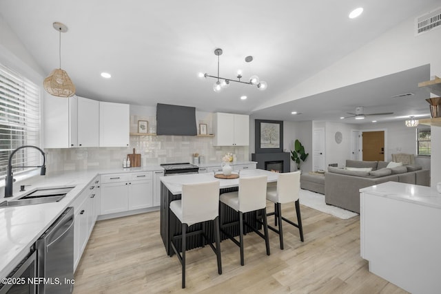 kitchen featuring pendant lighting, sink, wall chimney range hood, white cabinets, and a kitchen island