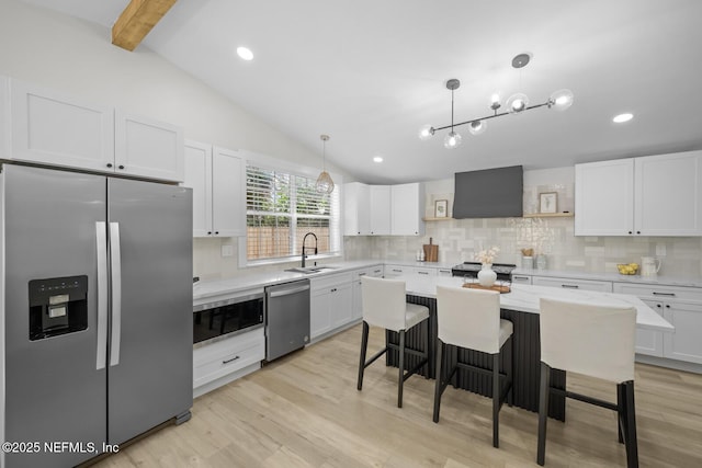 kitchen featuring appliances with stainless steel finishes, a breakfast bar, decorative light fixtures, white cabinets, and wall chimney exhaust hood