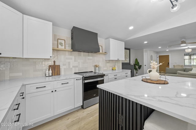 kitchen featuring electric stove, wall chimney range hood, white cabinetry, and light stone counters