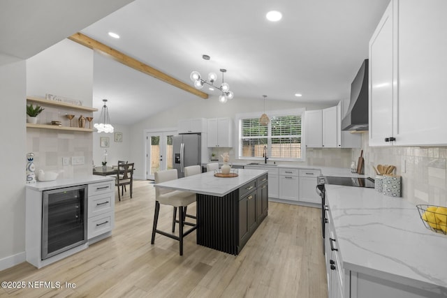 kitchen with wall chimney range hood, appliances with stainless steel finishes, white cabinetry, a center island, and wine cooler