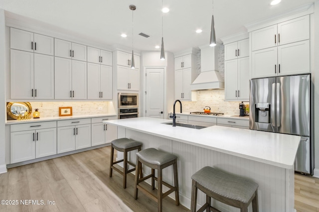 kitchen with white cabinetry, hanging light fixtures, a kitchen island with sink, and appliances with stainless steel finishes