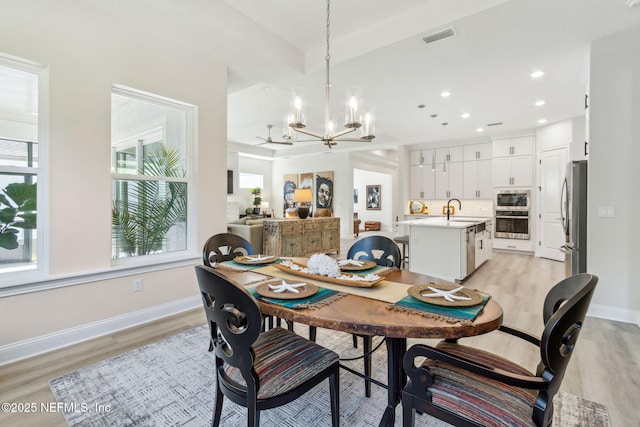 dining space featuring sink, light hardwood / wood-style flooring, and a chandelier