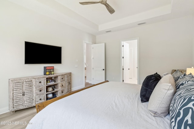 bedroom featuring light hardwood / wood-style flooring, ceiling fan, and a raised ceiling