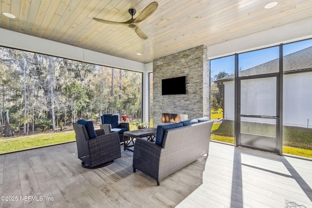 sunroom / solarium with ceiling fan, an outdoor stone fireplace, and wooden ceiling