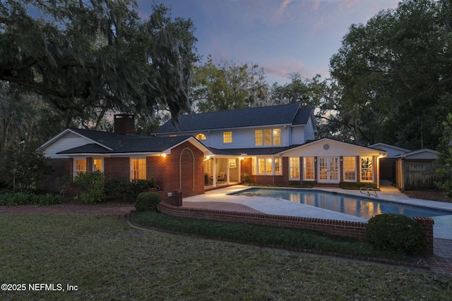 back house at dusk featuring a yard and a patio area