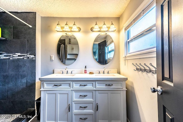 bathroom featuring a textured ceiling, tiled shower, and vanity