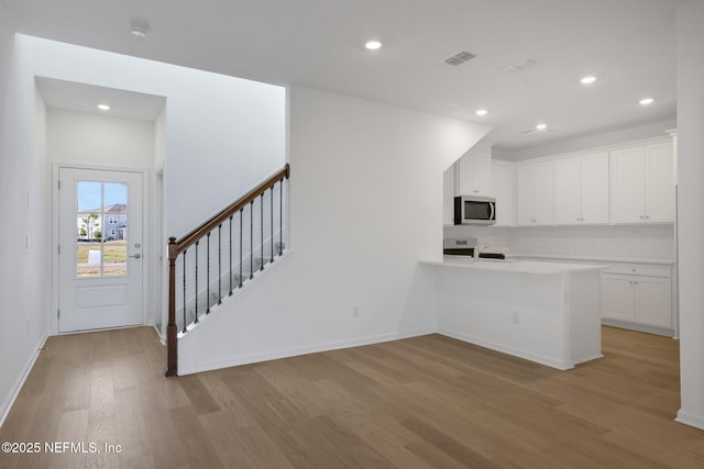 kitchen featuring white cabinetry, tasteful backsplash, range, light hardwood / wood-style flooring, and kitchen peninsula