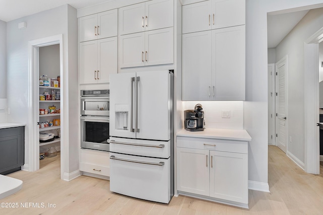 kitchen with high end fridge, stainless steel double oven, white cabinets, and light wood-type flooring