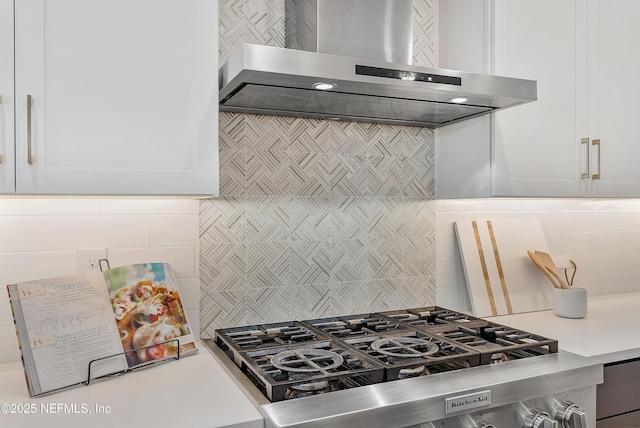 kitchen with stainless steel stove, stovetop, range hood, white cabinets, and decorative backsplash