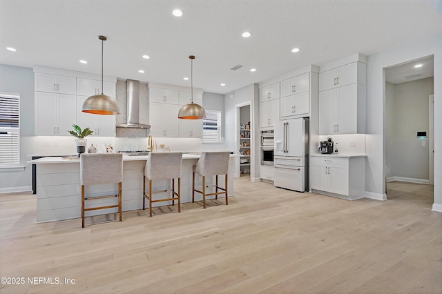 kitchen featuring white cabinets, high end fridge, hanging light fixtures, and wall chimney range hood