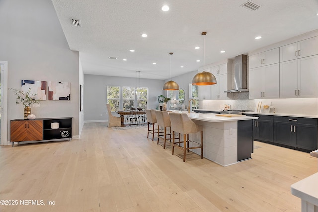 kitchen featuring a kitchen island with sink, decorative light fixtures, light hardwood / wood-style floors, and wall chimney exhaust hood