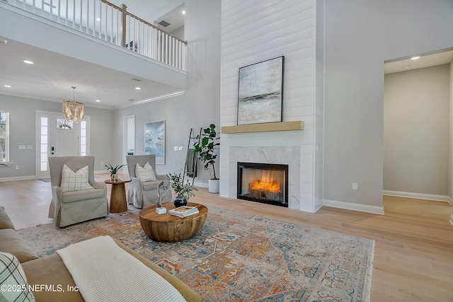 living room featuring crown molding, a fireplace, light hardwood / wood-style floors, and a towering ceiling