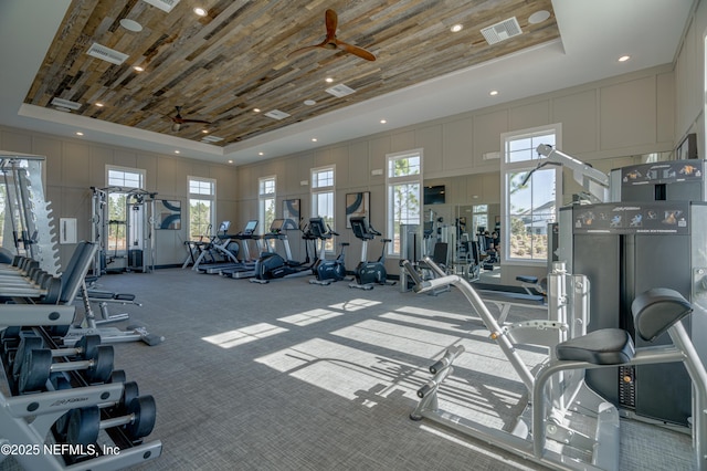 workout area with carpet flooring, a tray ceiling, ceiling fan, and a towering ceiling