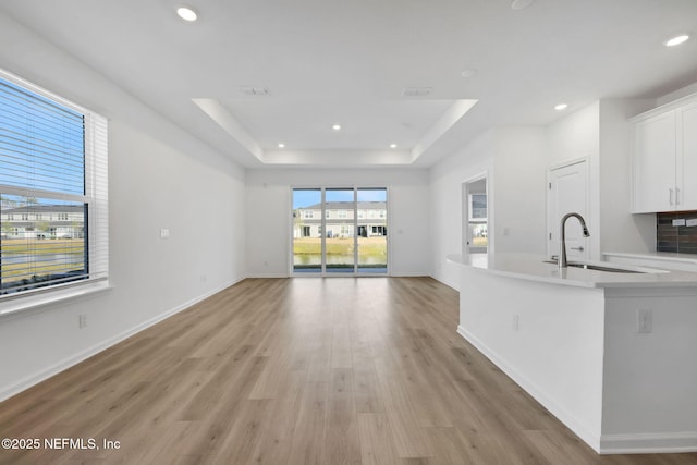 kitchen featuring sink, white cabinets, light wood-type flooring, and a tray ceiling