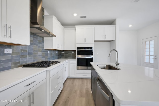 kitchen with sink, white cabinetry, stainless steel appliances, light stone countertops, and wall chimney range hood