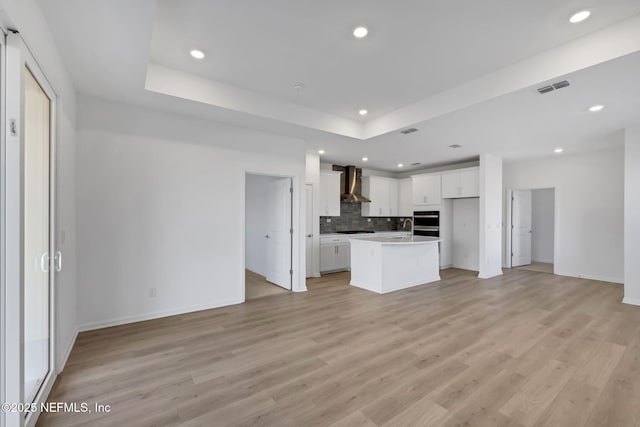 kitchen featuring white cabinets, a tray ceiling, a center island, and wall chimney range hood