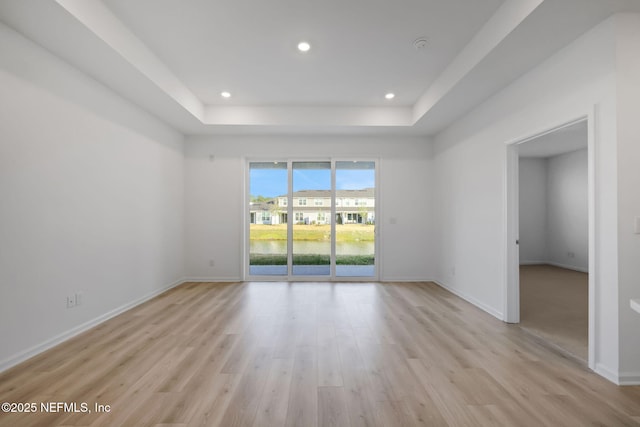 empty room featuring light hardwood / wood-style floors, a raised ceiling, and a water view