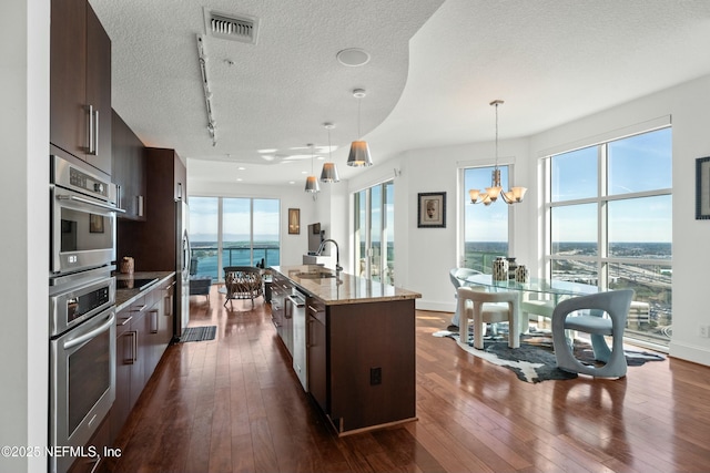 kitchen featuring dark brown cabinets, decorative light fixtures, and a kitchen island with sink