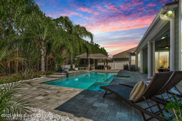 pool at dusk featuring a ceiling fan, a patio, fence, and an outdoor pool