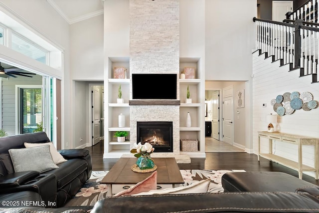 living area featuring ornamental molding, wood finished floors, a towering ceiling, a stone fireplace, and ceiling fan