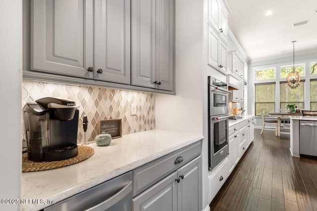 kitchen with light stone counters, an inviting chandelier, gray cabinets, appliances with stainless steel finishes, and tasteful backsplash