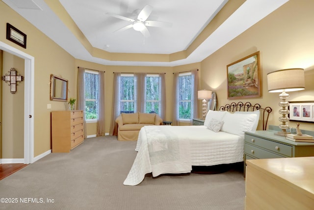 bedroom with ceiling fan, light colored carpet, and a raised ceiling