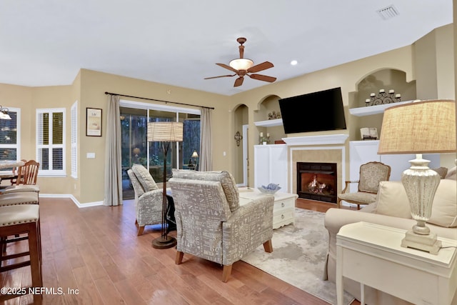 living room featuring built in features, light wood-type flooring, and ceiling fan