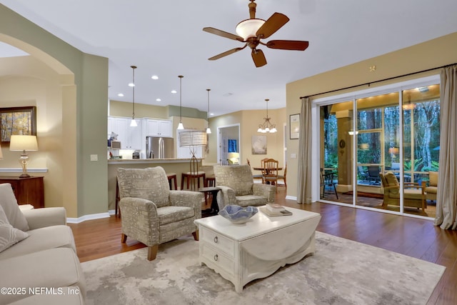 living room with light wood-type flooring and ceiling fan with notable chandelier