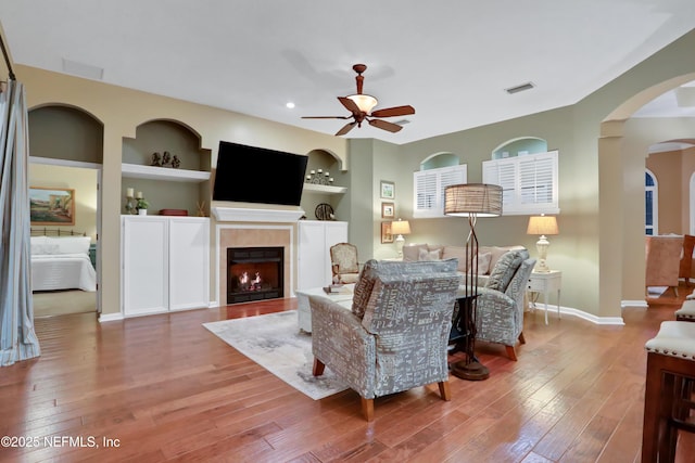 living room featuring built in shelves, ceiling fan, a tile fireplace, and hardwood / wood-style flooring