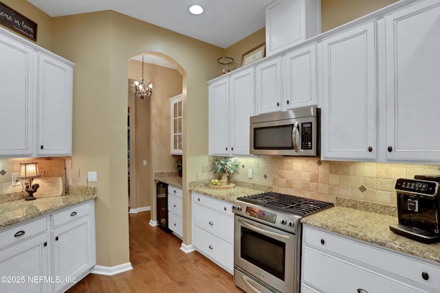 kitchen with light stone countertops, appliances with stainless steel finishes, white cabinets, light hardwood / wood-style flooring, and pendant lighting