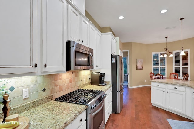 kitchen featuring white cabinets, stainless steel appliances, decorative backsplash, hanging light fixtures, and light stone counters