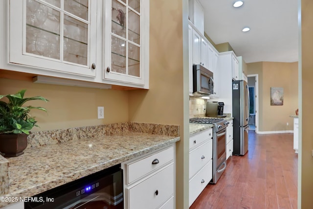 kitchen featuring light stone countertops, appliances with stainless steel finishes, white cabinetry, decorative backsplash, and hardwood / wood-style flooring