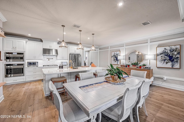 dining space featuring light hardwood / wood-style floors, a textured ceiling, and crown molding