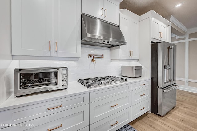 kitchen featuring ornamental molding, white cabinets, light wood-type flooring, and stainless steel appliances