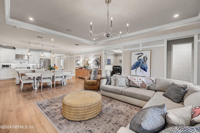 living room featuring a tray ceiling, light hardwood / wood-style flooring, ornamental molding, and a chandelier