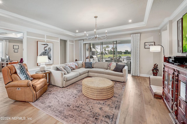 living room featuring crown molding, light wood-type flooring, a notable chandelier, and a tray ceiling