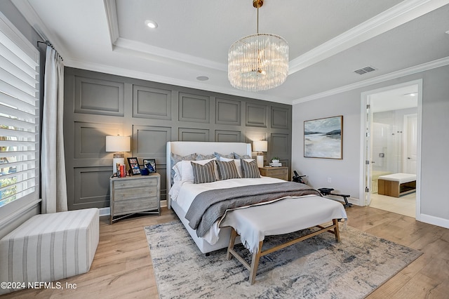 bedroom with connected bathroom, an inviting chandelier, a raised ceiling, light hardwood / wood-style flooring, and crown molding