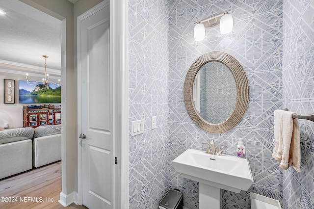 bathroom with wood-type flooring, an inviting chandelier, sink, tile walls, and crown molding