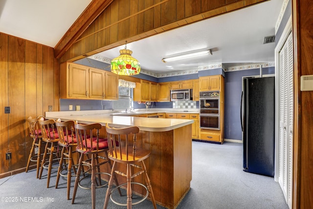 kitchen with a kitchen bar, light carpet, wooden walls, kitchen peninsula, and black appliances