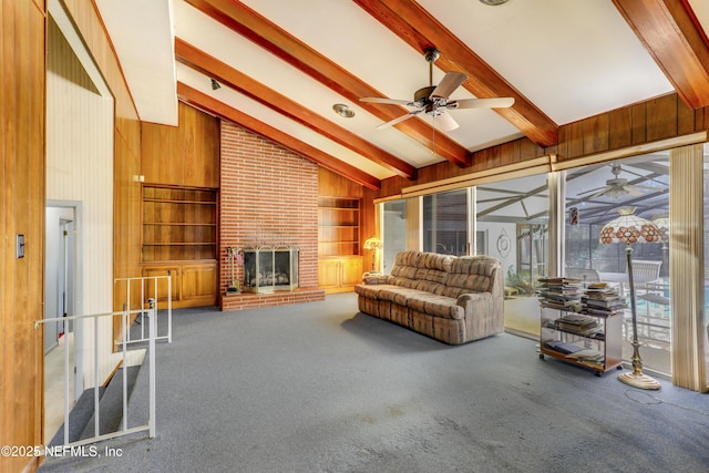 living room featuring wooden walls, carpet, a brick fireplace, beam ceiling, and built in shelves