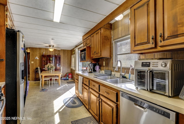 kitchen with appliances with stainless steel finishes, sink, ceiling fan, and wood walls