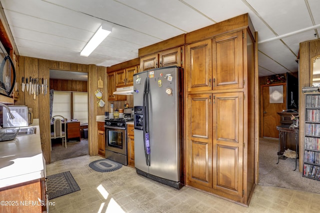 kitchen with appliances with stainless steel finishes, sink, light colored carpet, and wood walls