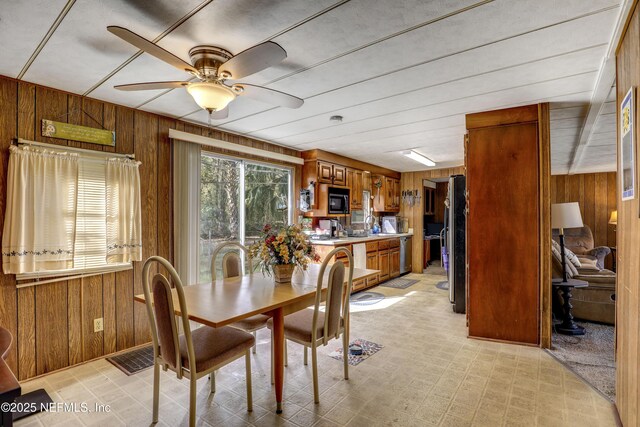 dining space with ceiling fan and wooden walls