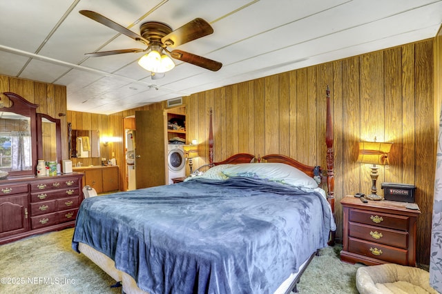 bedroom with light carpet, washer / dryer, wooden walls, and ceiling fan