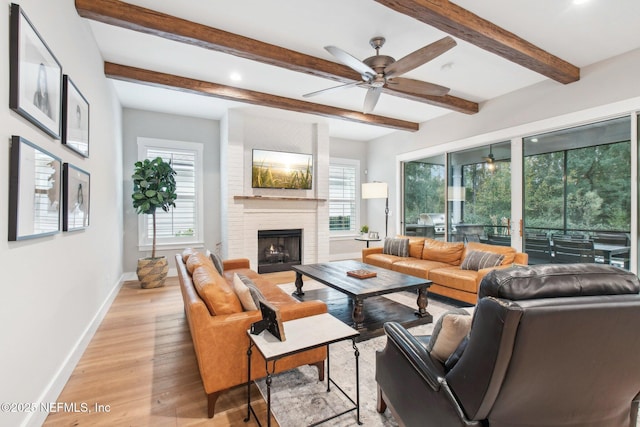 living room with a brick fireplace, beam ceiling, light hardwood / wood-style flooring, and a healthy amount of sunlight