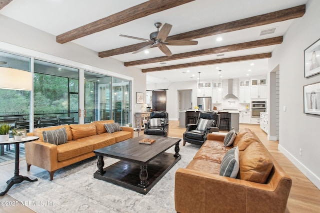 living room featuring ceiling fan, beam ceiling, light hardwood / wood-style floors, and a healthy amount of sunlight