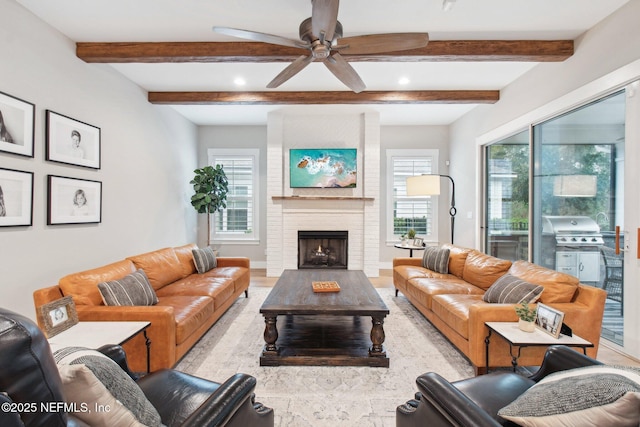 living room featuring beamed ceiling, ceiling fan, a wealth of natural light, and a fireplace