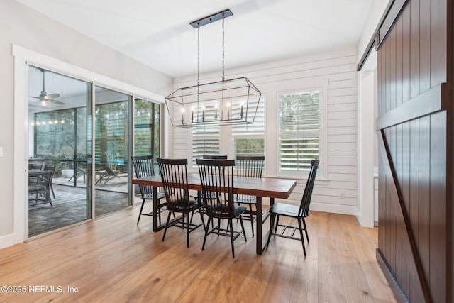 dining area with ceiling fan with notable chandelier, light hardwood / wood-style flooring, and wood walls