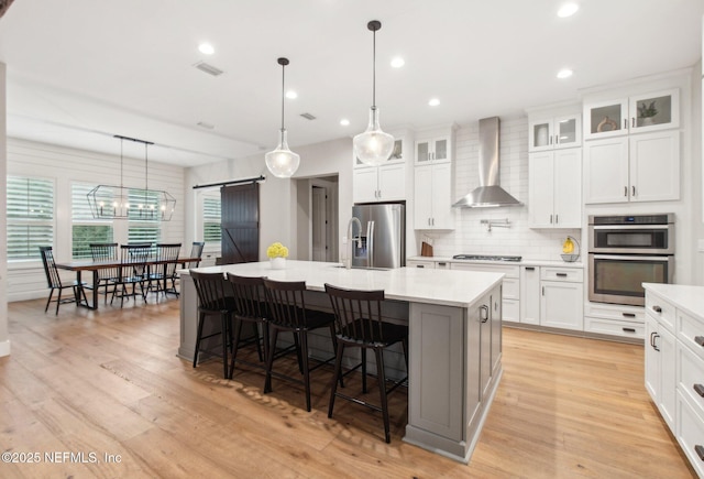 kitchen featuring appliances with stainless steel finishes, pendant lighting, wall chimney exhaust hood, a barn door, and a spacious island