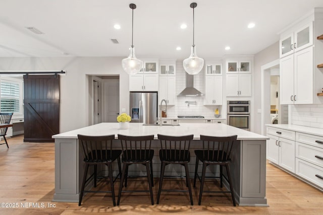 kitchen with a kitchen breakfast bar, a large island, stainless steel appliances, a barn door, and wall chimney exhaust hood